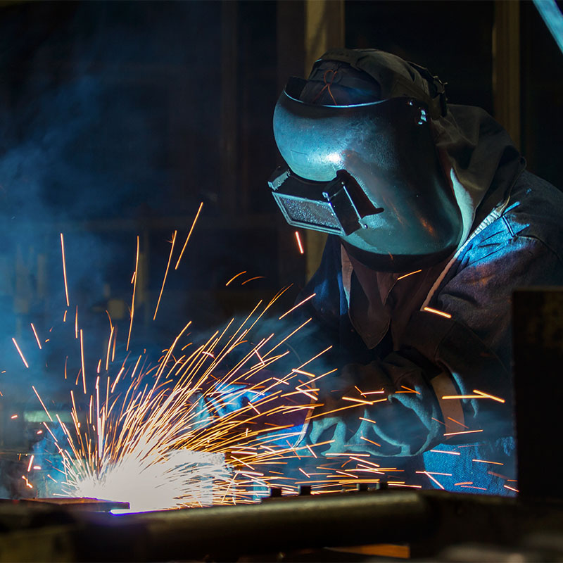 Worker with protective mask welding automotive part in factory